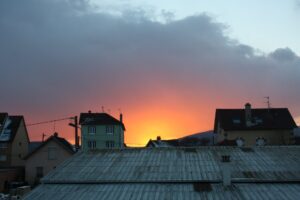 [Justine CM] Coucher de soleil orange tirant sur le gris à cause des nuages, au-dessus des toits