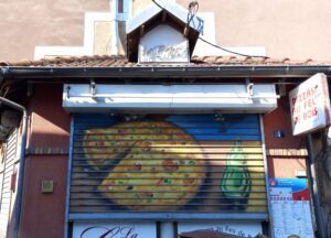 [Justine CM] Belfort, pas loin du Marché des Vosges. Photo prise en juillet 2022. volet roulant d'une pizzeria, qui représente une pizza et une bouteille de soda verte à côté.