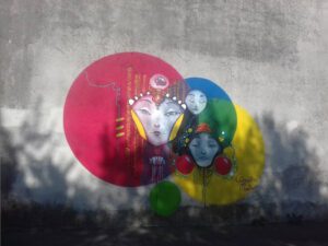 [Justine CM] Belfort, vers la rue Jean Jaurès. Photo prise en 2019, là où j'ai rencontré l'artiste Clémentine Martinez. Trois ronds de couleur jaune, bleu et rouge se croisent, forment du vert, et trois têtes de femmes d'inspiration japonaise. Un petit rond vers en bas.