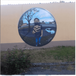 [Justine CM] Belfort, Résidences. Photo prise en 2019. Bulle où il y a un effet miroir du parking vers lequel il a été dessiné, avec un homme qui se tient devant avec un téléphone portable, comme pour prendre en photo.