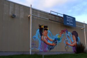 [Justine CM] Belfort, Glacis. Photo prise en avril 2021. Deux enfants jouent avec un tube de peinture et un pinceau grandeur nature. Peinture multicolore. L'un des deux enfants tient un doudou en forme d'ours. Bulles bleues en fond.