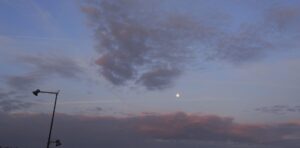 Ciel gris, nuageux, aux nuages parcourus d'un rose léger, et la lune visible même en plein jour. Poteau électrique à gauche. Prise à la Gare TGV de Meroux-Moval.