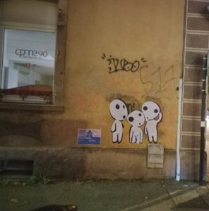 Trois kodamas (créatures de Princesse Mononoké) sur un mur. Ce sont des autocollants, pas du streetart pur. Photo prise fin 2022.