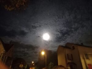 Ciel noir et nuageux, où l'on voit la pleine lune. Lampadaire diffusant une lumière jaune.