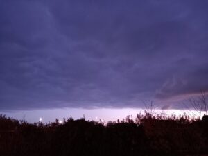 Ciel d'un bleu teinté de gris et de violet côté front nuageux, qui s'arrête net au loin. Bande plus claire sans nuages ensuite.