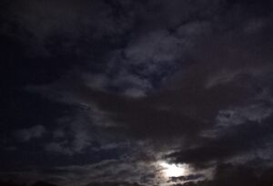 Ciel de nuit très nuageux, avec la lune qui se montre derrière les nuages.